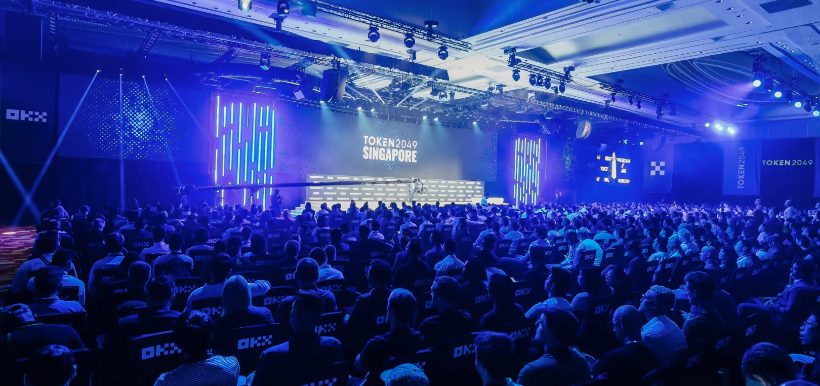 Large audience seated in a conference hall with a stage displaying 'TOKEN2049 SINGAPORE' under blue lighting.